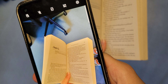 Dekoratives Bild von einem Handy, mit dem ein Foto von einem Buch gemacht wird