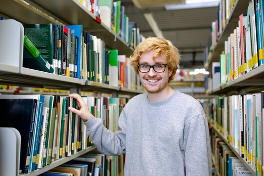 Student stands at a bookshelf in the library.
