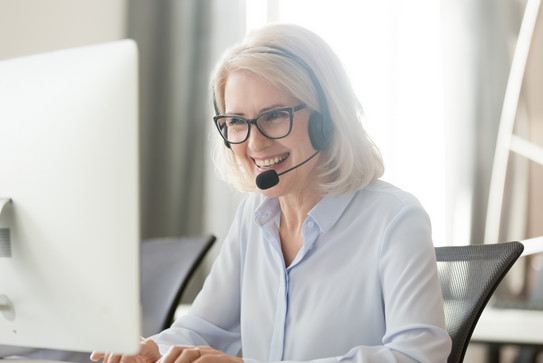 Eine Frau sitzt vor ihrem Laptop und trägt ein Headset. 