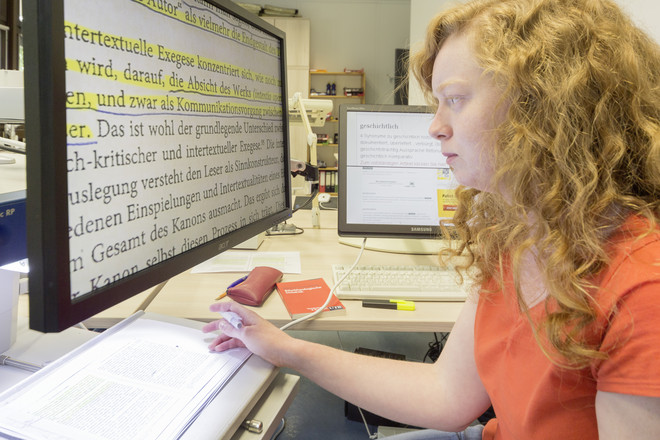 Eine Studentin sitzt an einem Computer und liest einen Text in großer Schrift.