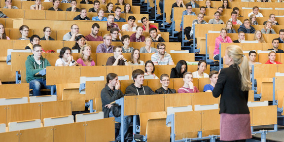 Eine Dozierende steht vor Studierenden in der Vorlesung im Hörsaal. 