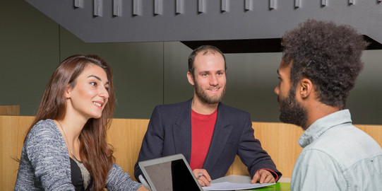 Three students sit opposite each other and they are talking.